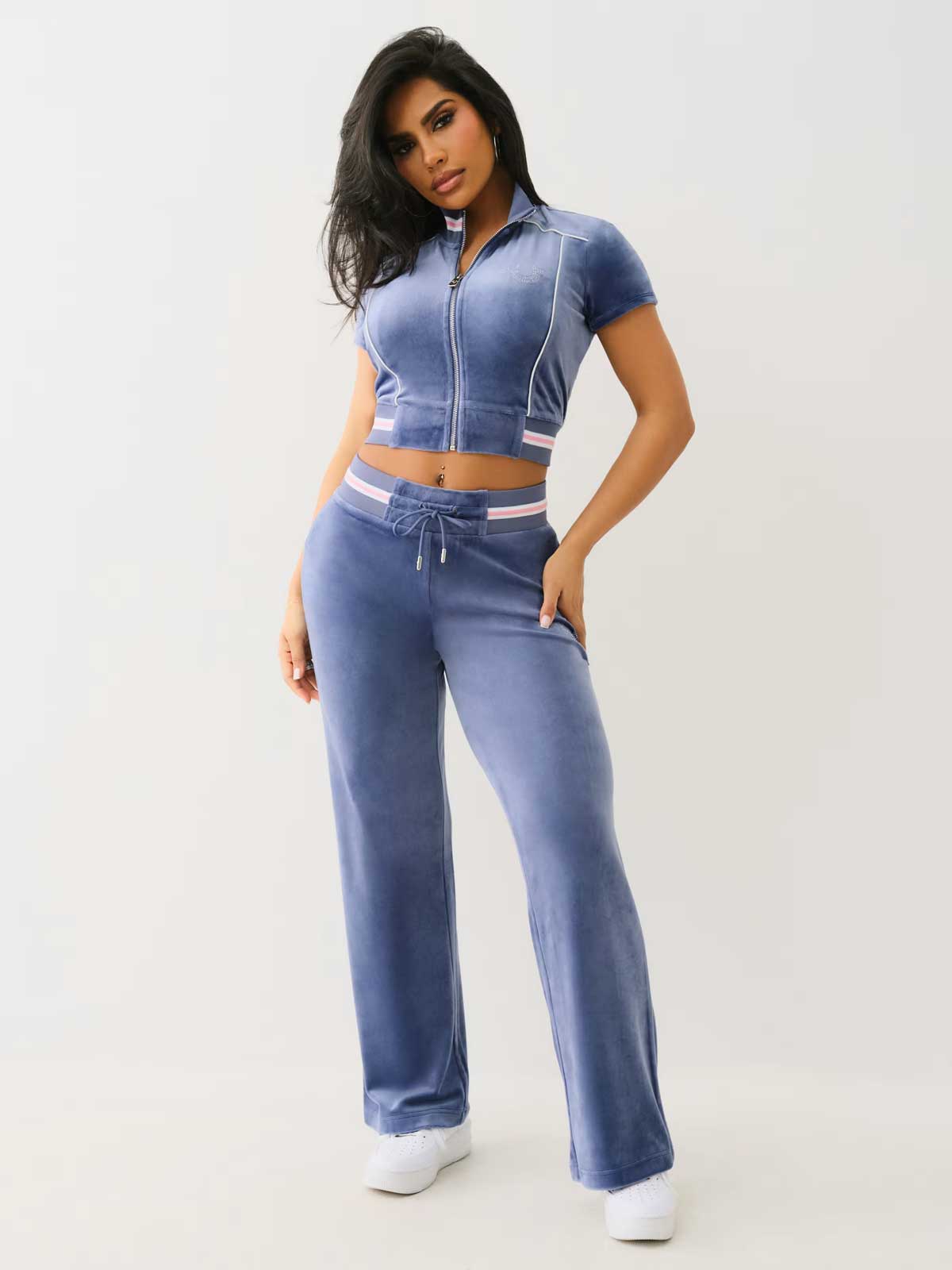 Woman wearing a blue velvet matching set, with a zip up short sleeve top and wide leg pant bottom