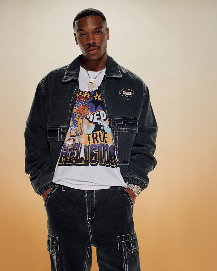Man wears true religion black cargo pants with white stitching, a black true religion jacket with white stitching, and a white graphic tee