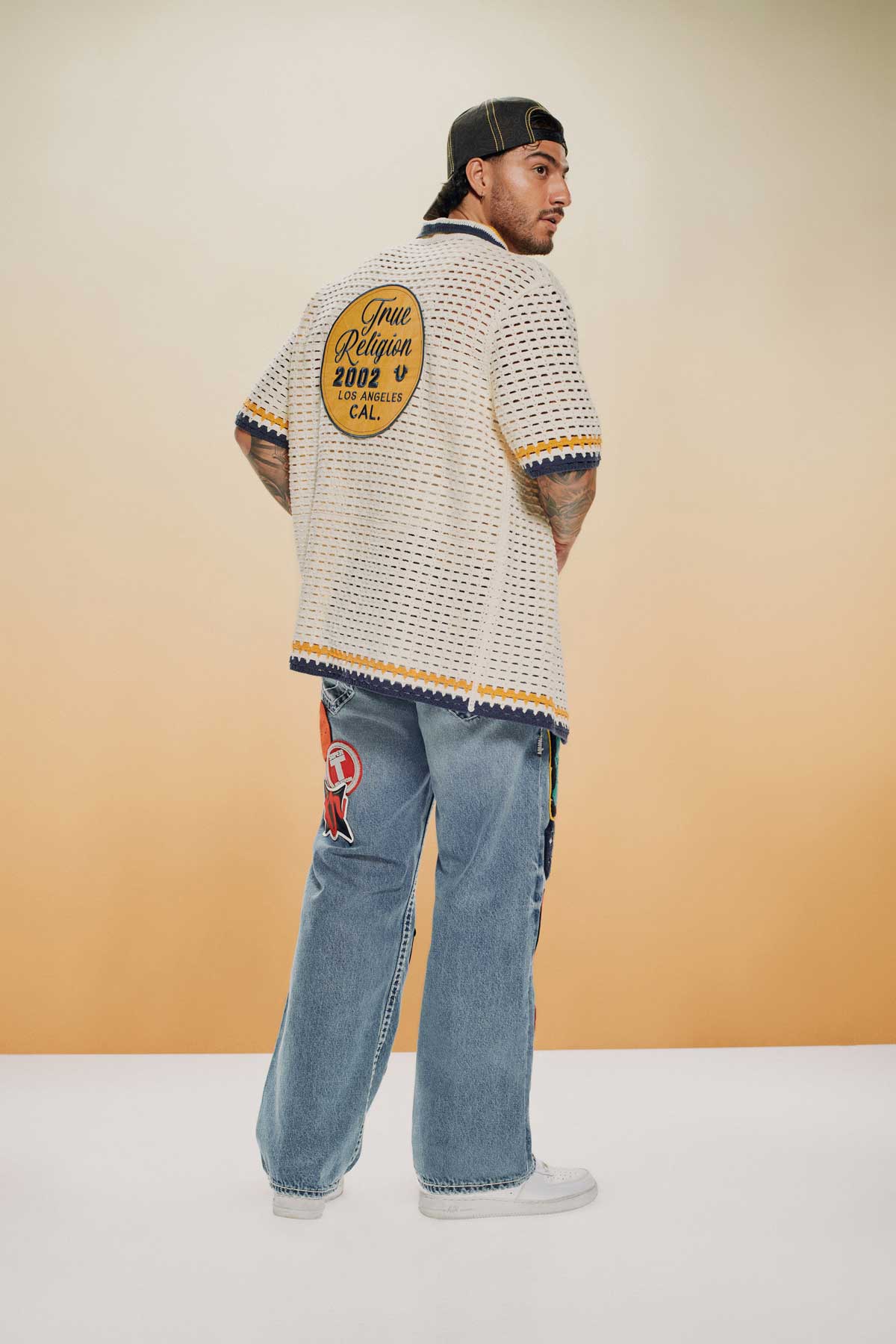 Man wears a true religion white knit short sleeve top and true religion light wash jeans