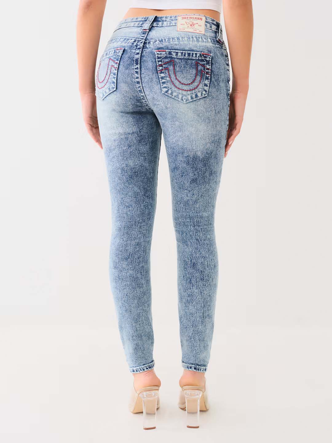 Woman wearing acid wash skinny jeans with horseshoe stitching and clear high heels