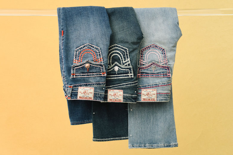three pairs of true religion jeans in different washes with pink, white, and red stitching