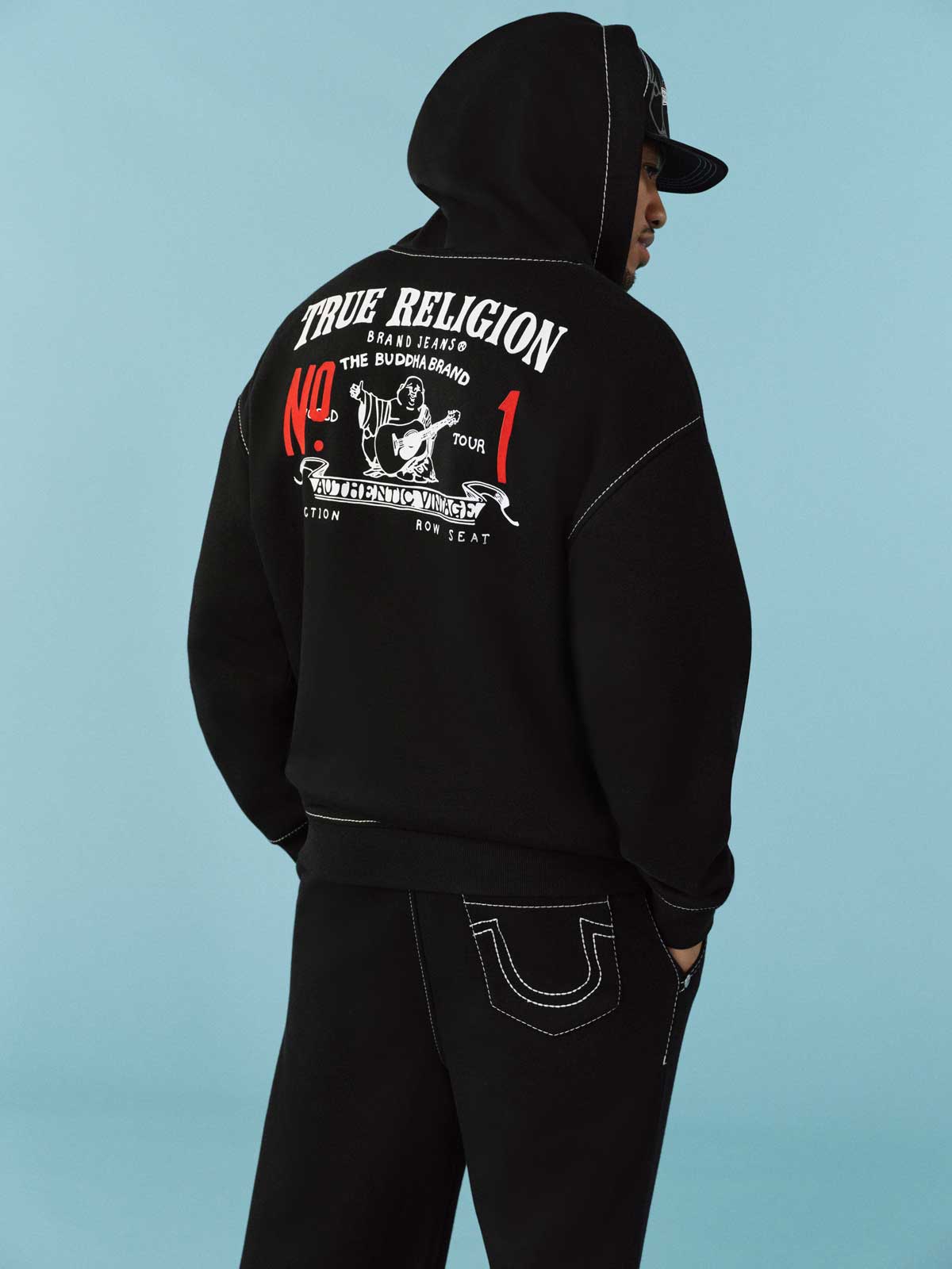 Man wears true religion black hoodie with white detailing and true religion black jeans with white stitching