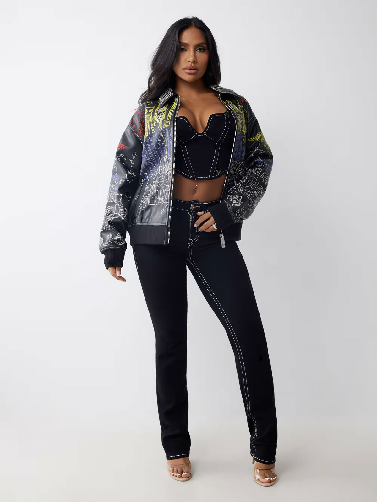 Woman wears an embroidered oversized faux leather jacket, a denim corset top, and dark wash jeans 