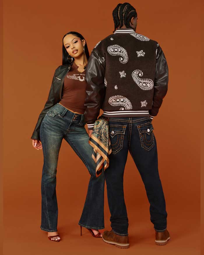 Woman wears true religion brown baby tee with true religion dark wash flared jeans, and man wears true religion brown paisley varsity jacket and true religion dark wash baggy jeans with stitching