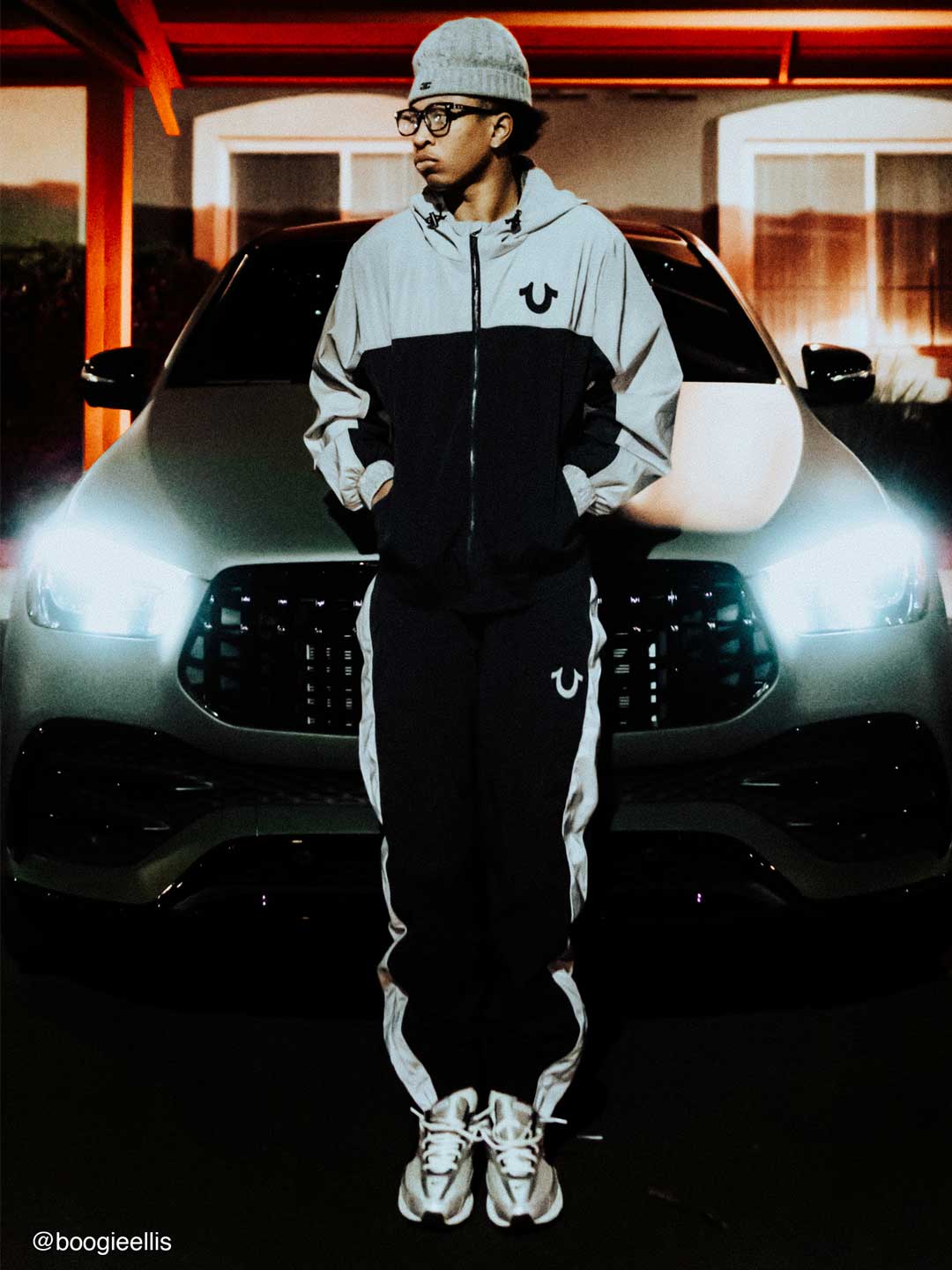 Man stands in front of a black car wearing a true religion black and white sweat set