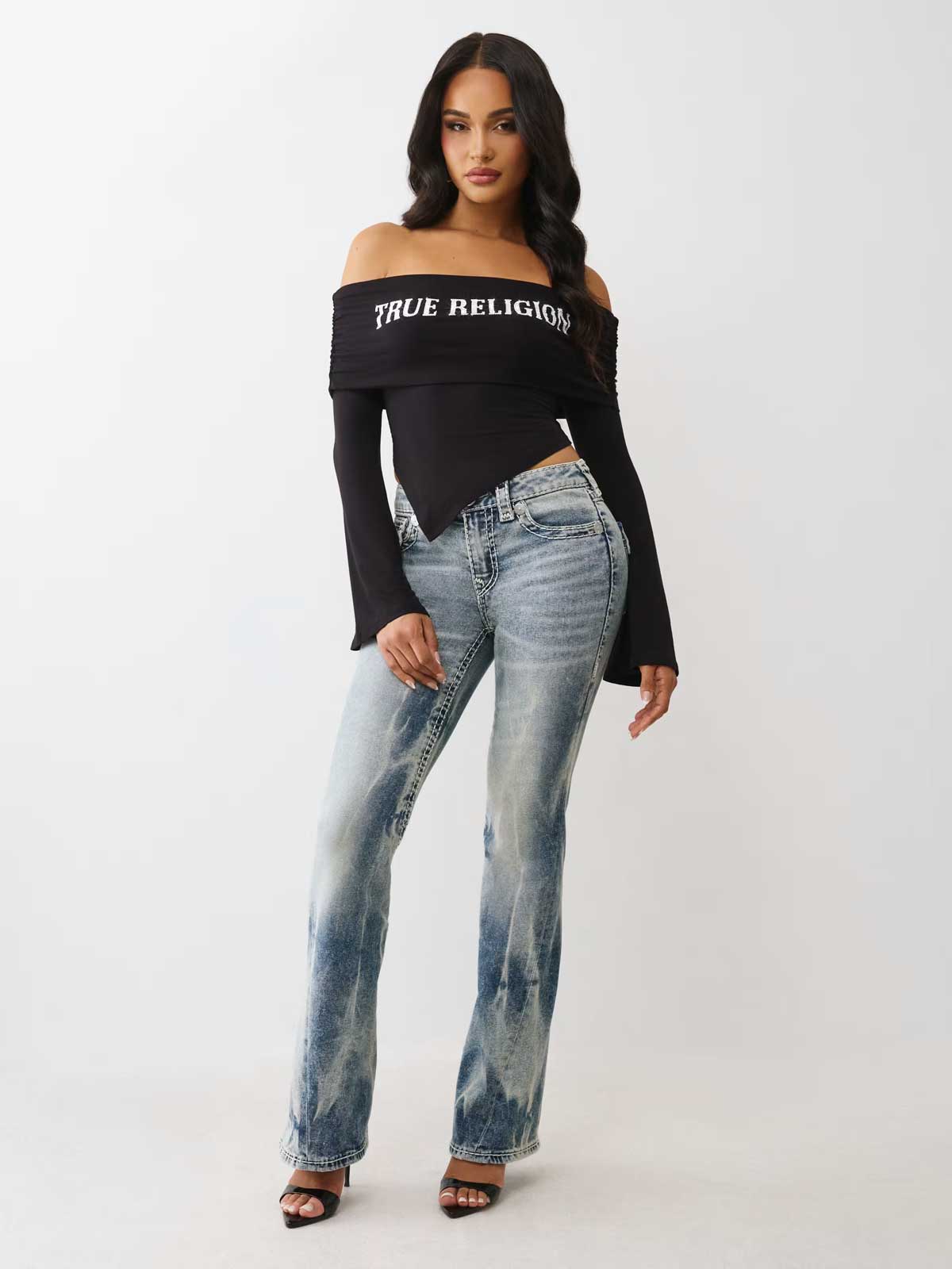 woman wearing true religion asymmetric of the shoulder long sleeve top with joey mid rise super t flare jeans