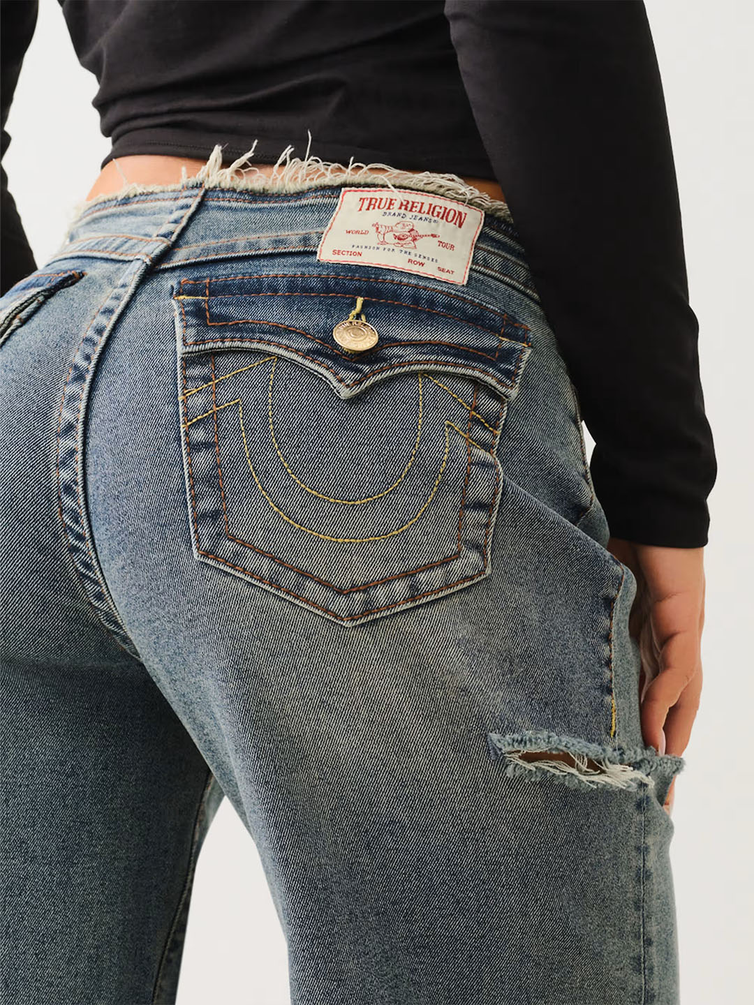 Close up of true religion medium wash raw edge denim with yellow stitching