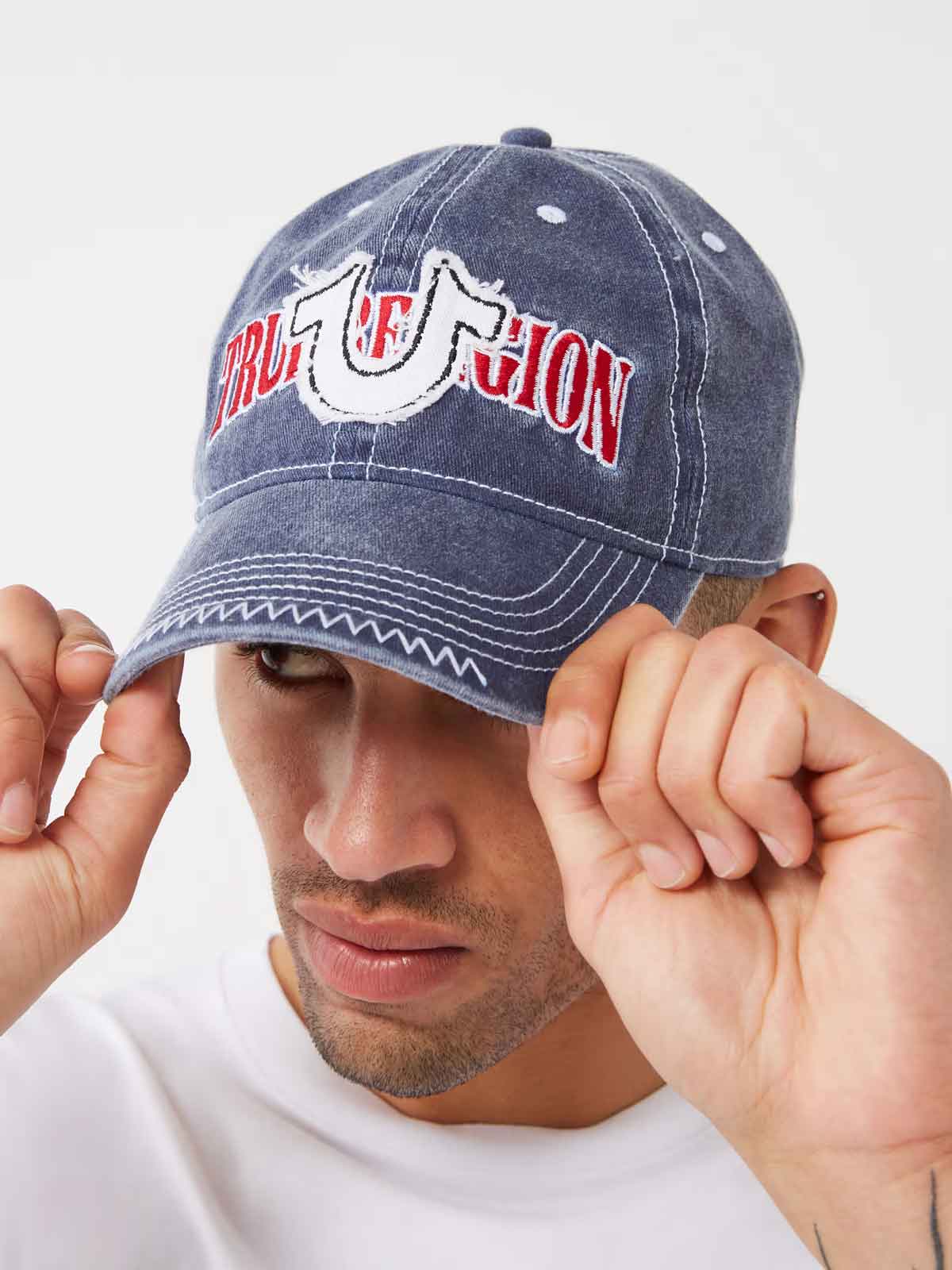 Man wears a true religion gray baseball cap with true religion horseshoe stitching on the front