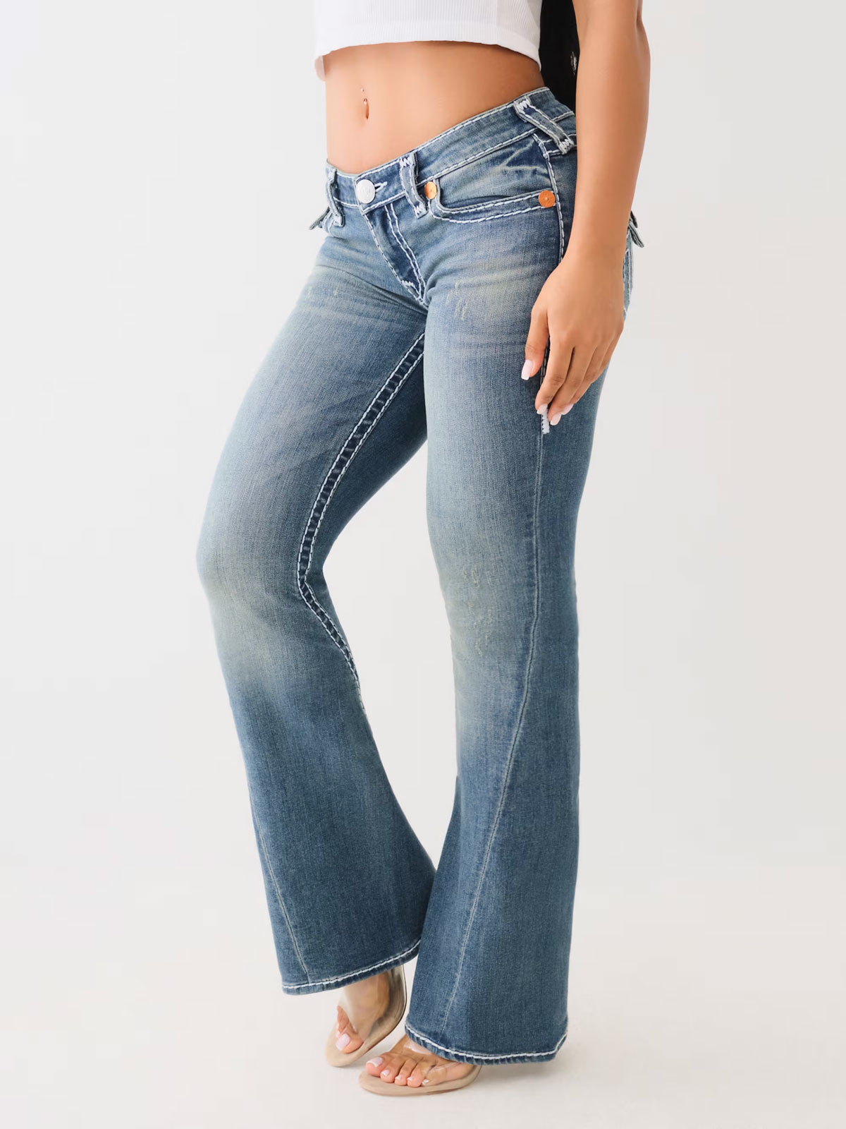 Woman wearing True Religion medium wash boot cut jeans with a zipper hem and clear high heels