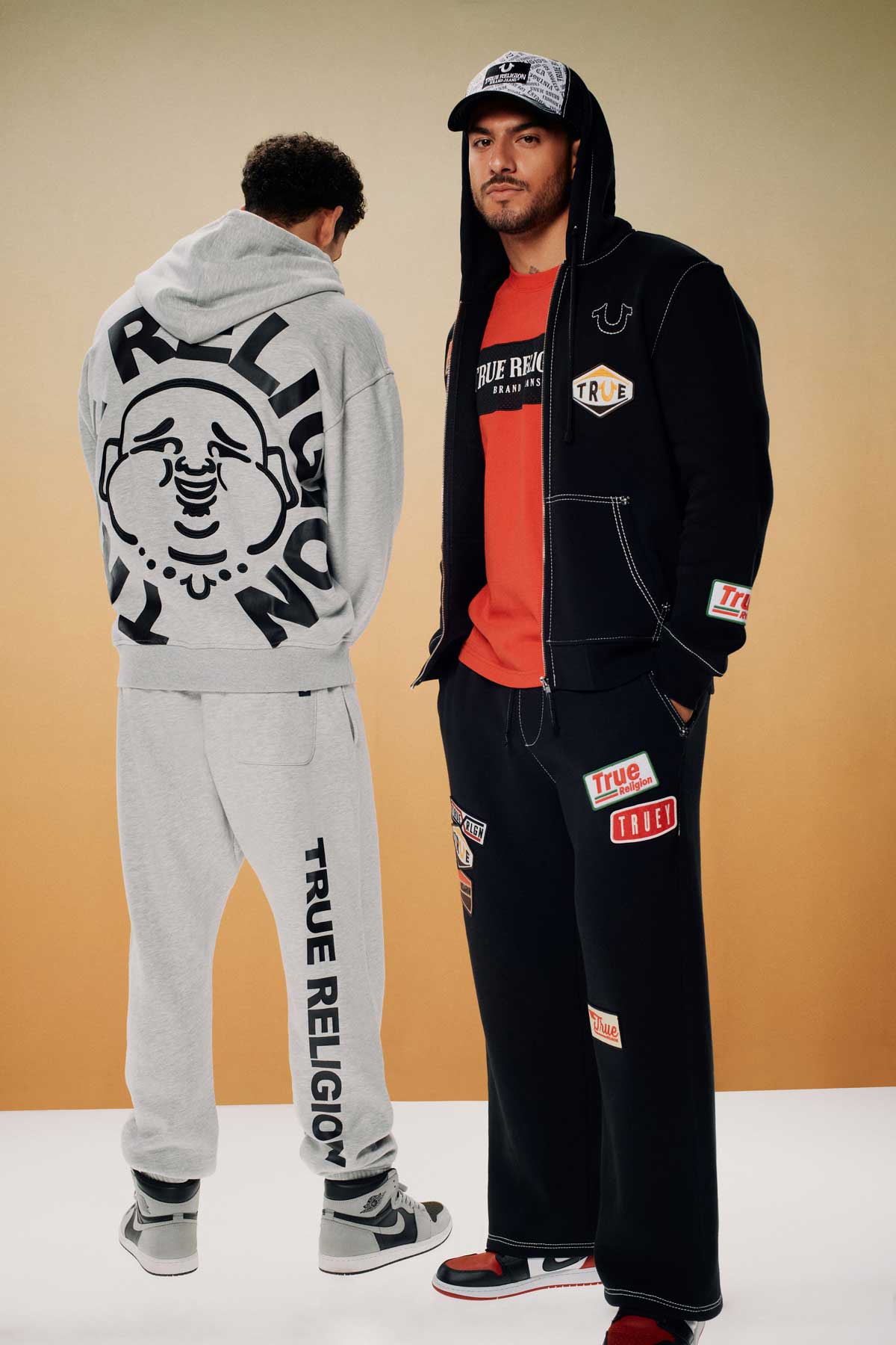 Two men wear true religion sweat sets; one wears a gray sweat set with black details, another a black sweat set with white and red stitching