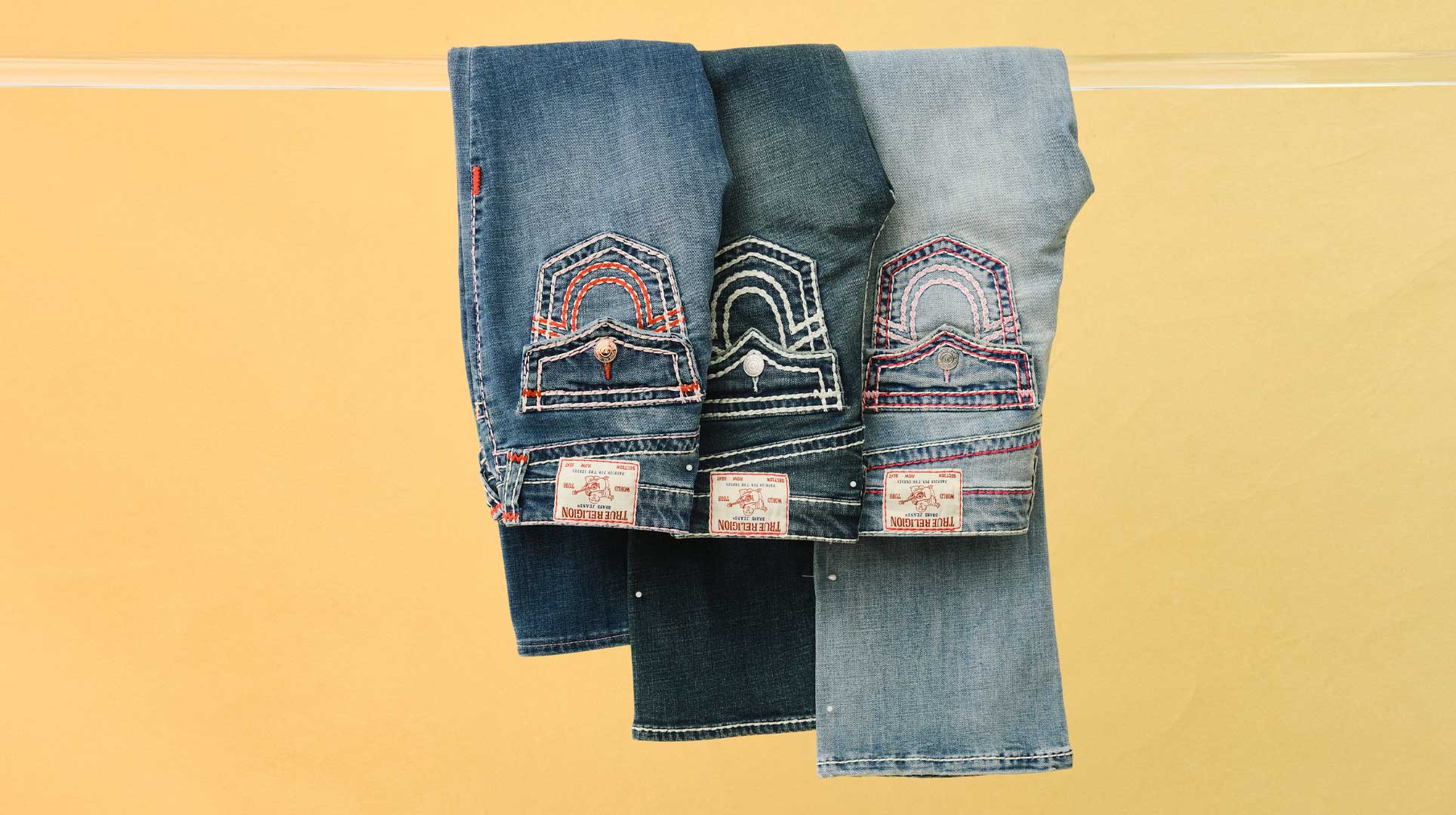 three pairs of true religion jeans in different washes with pink, white, and red stitching