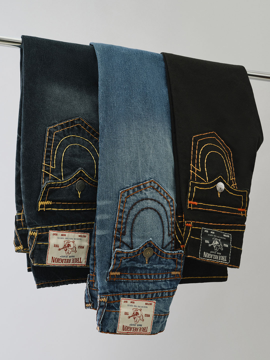 Three pairs of folded true religion jeans with horseshoe stitching on the pockets.