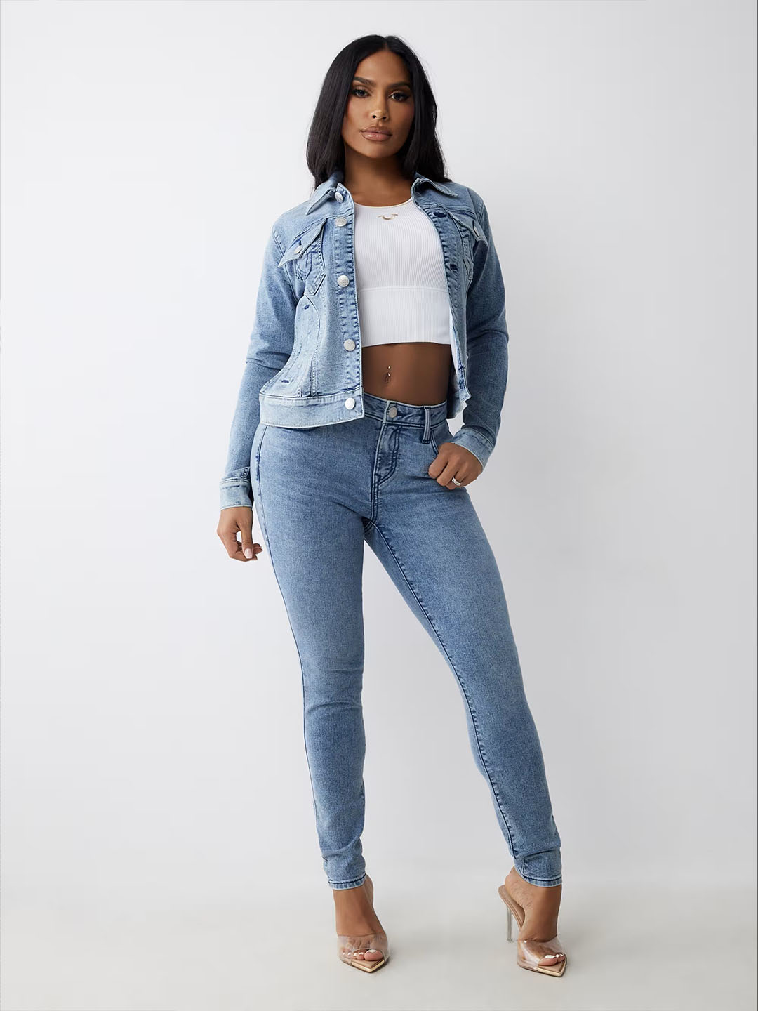 Woman wearing a true religion light wash denim jacket, white t shirt, and true religion blue skinny jeans.